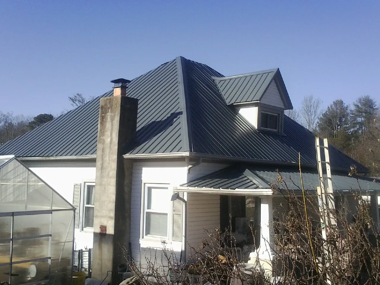 Dark blue standing seam metal roof on a white farmhouse with dormer — Slate & Tile Roof Repair by Roofing Brothers in Markesan