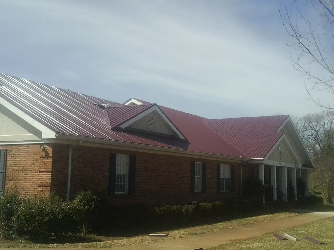 Red metal roof with gabled entries on a long brick building, from a Hail Damage Roof Repair job in Markesan