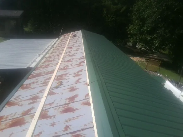 Old rusted panels beside newly installed green metal roofing — Wind Damage Roof Repair by Roofing Brothers in Markesan