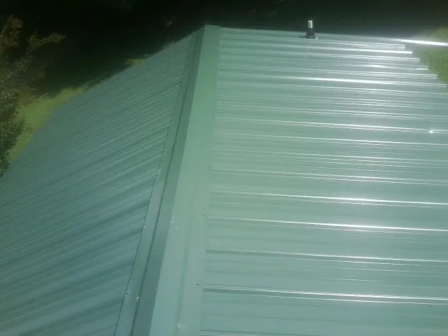 New green metal panels meeting at the ridge of a roof — Flat Roof Repair work by our crew in Markesan