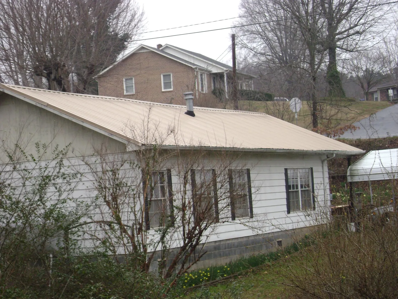 Tan metal roof on a white sided house set into a hillside — Commercial Roofing by Roofing Brothers in Markesan